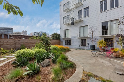 A white building with a balcony and a patio with chairs and plants.