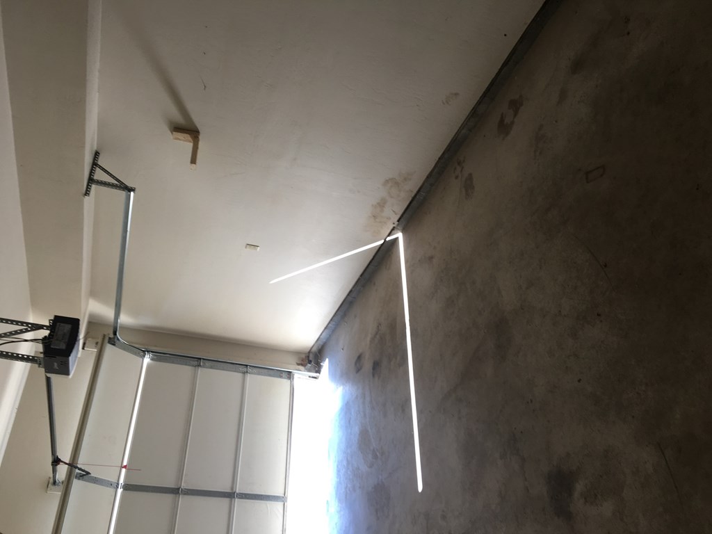 A white wall with a black object hanging from the ceiling.