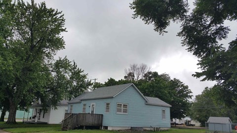 a blue and white house with trees and a cloudy sky