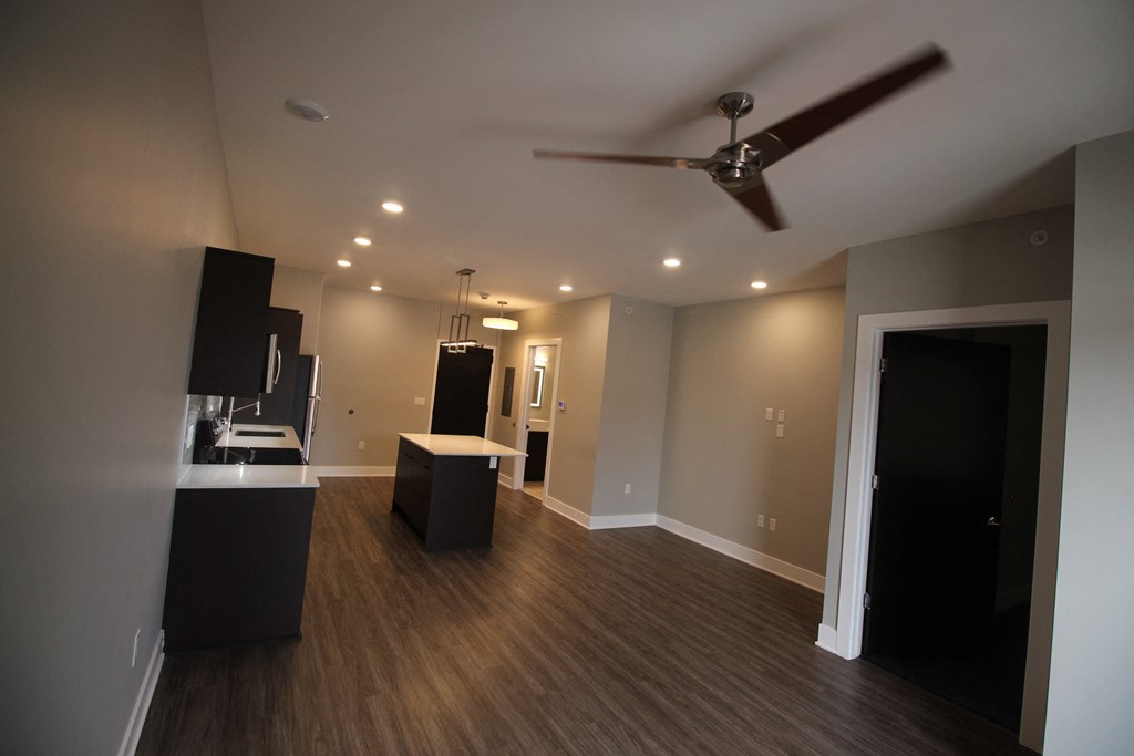 an empty living room with a ceiling fan and a kitchen