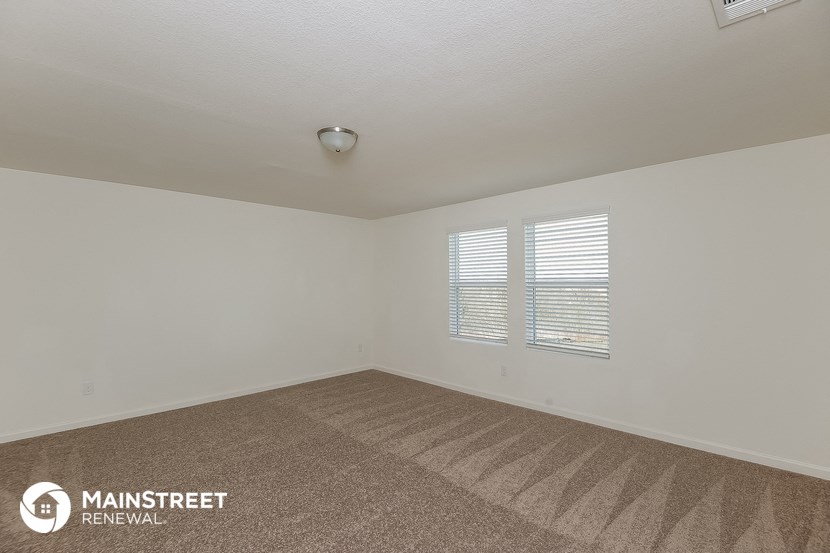 the living room of an apartment with carpet and two windows