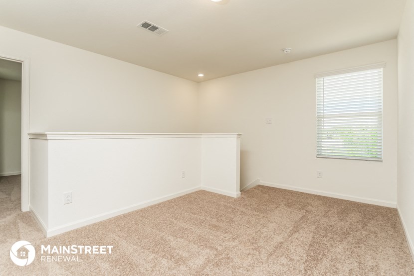 the spacious living room with white walls and carpeting and a window