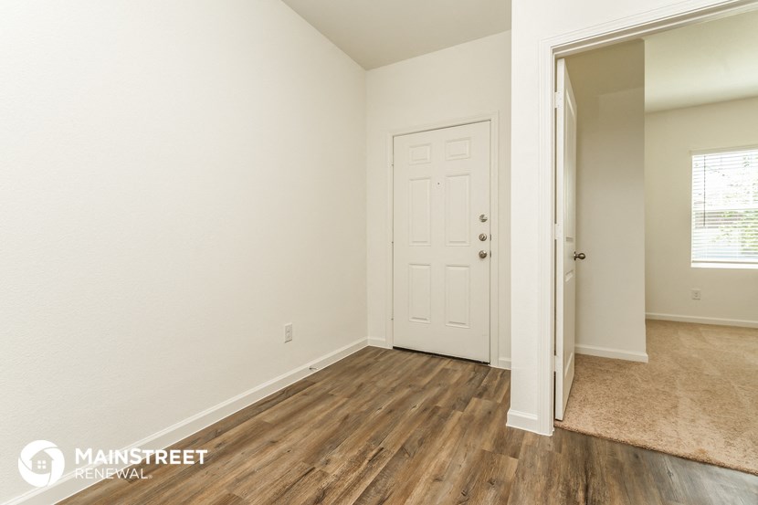 the spacious living room with wood flooring and a door to the bedroom