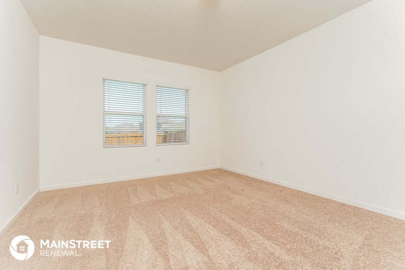 a spacious living room with carpet and two windows