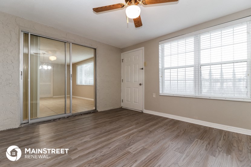 the living room of a home with a mirrored closet and a ceiling fan