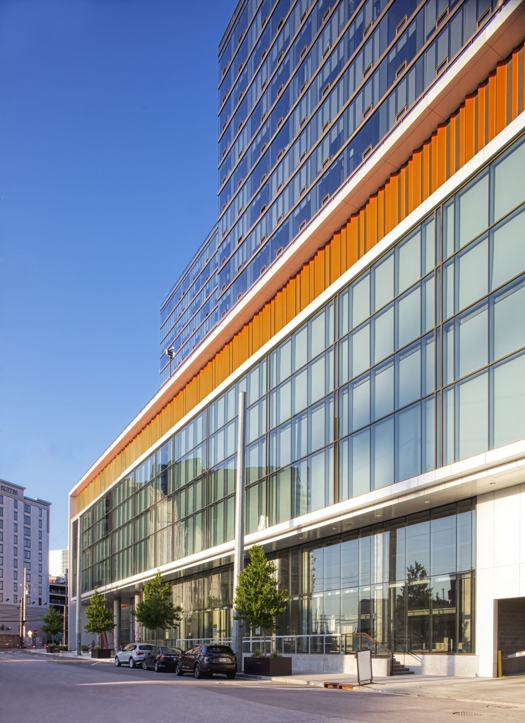 A modern building with a glass facade and a white and orange stripe at the top.