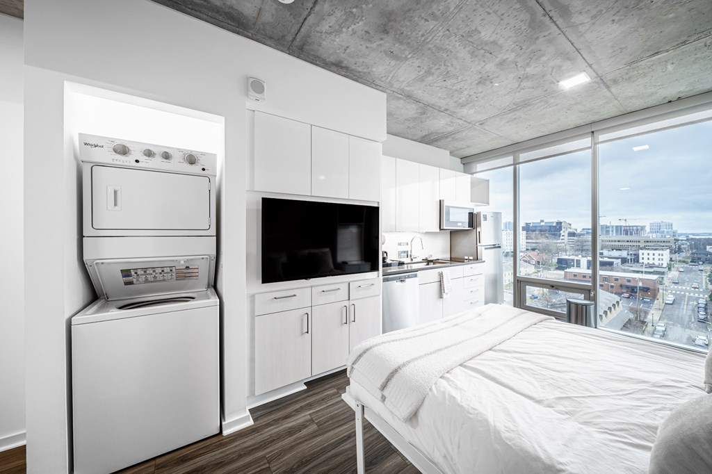 A modern bedroom with a large bed and a kitchen area with a washing machine and a refrigerator.