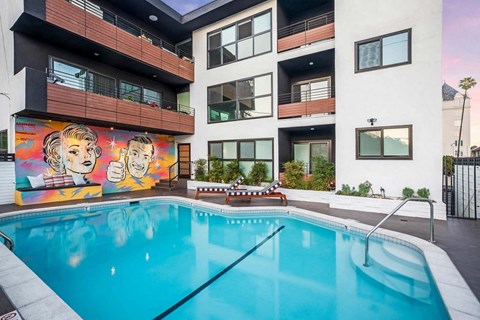 A mural of two people is on the side of a building next to a pool.