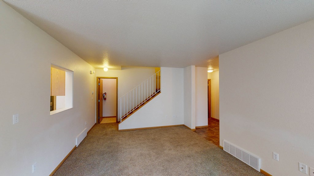 the living room and dining room of an apartment with carpeted floors and white walls