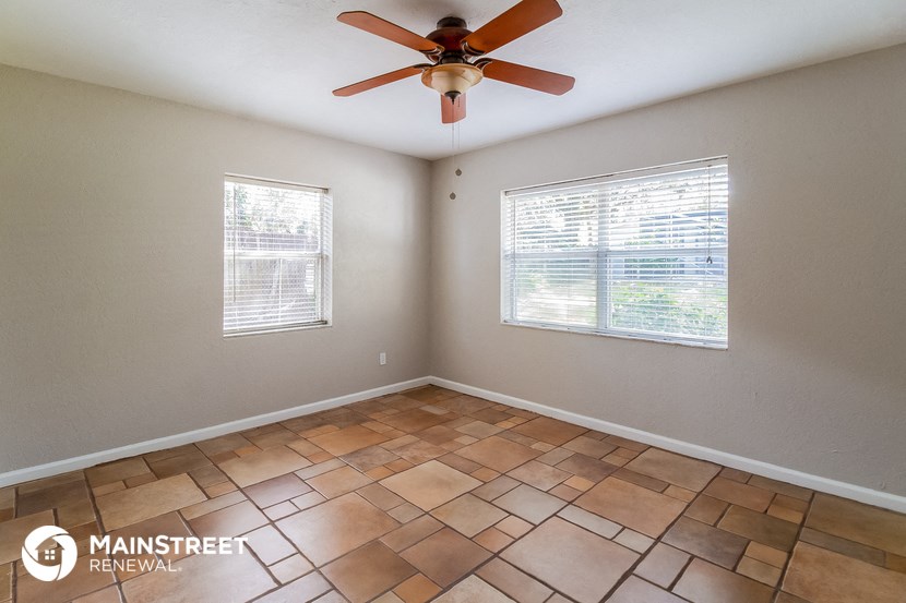 an empty living room with a ceiling fan and two windows