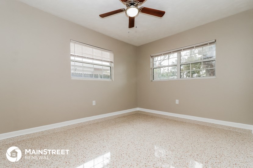 an empty room with a ceiling fan and two windows