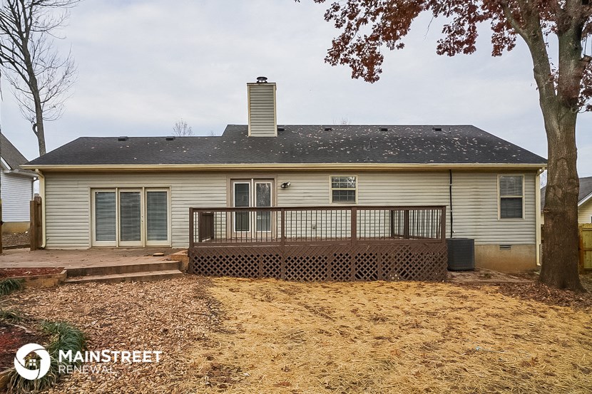 the back of a white house with a deck and a tree