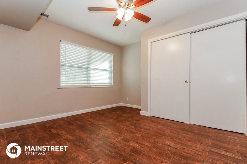 the bedroom of an apartment with wood floors and a ceiling fan