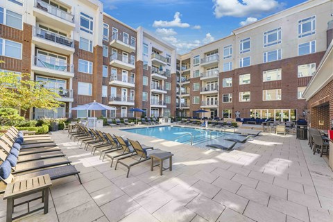 A large outdoor pool area with sun loungers and umbrellas in front of apartment buildings.