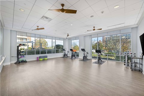 A spacious gym with a variety of exercise equipment and a view of the outdoors through large windows.