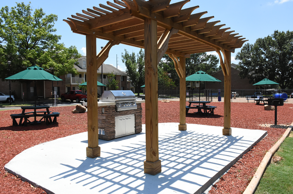 A wooden pavilion with a white base is in the middle of a park.