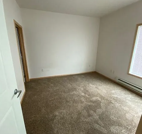 A room with a carpeted floor and a window with blinds.