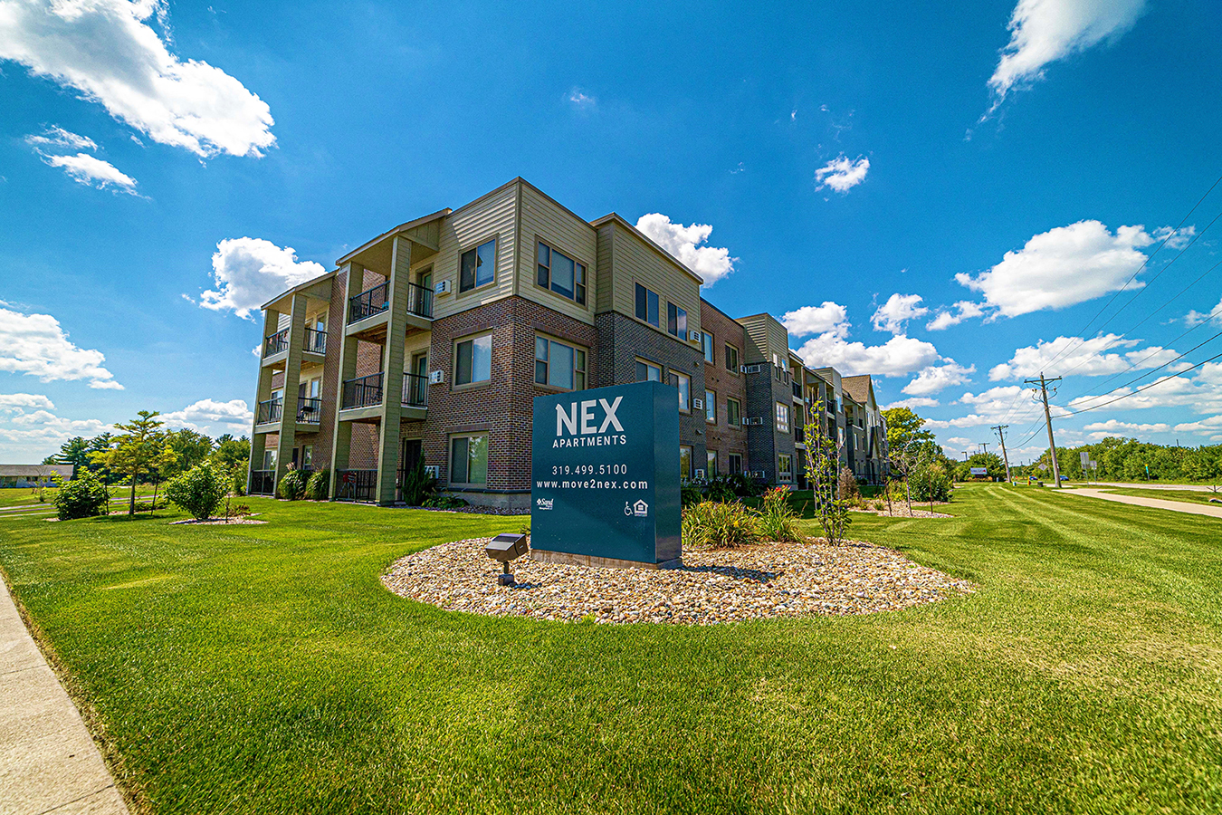 an apartment building with a sign in front of it on a green lawn