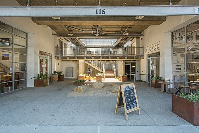 The image shows a spacious lobby with a staircase, a signboard, and a few potted plants.