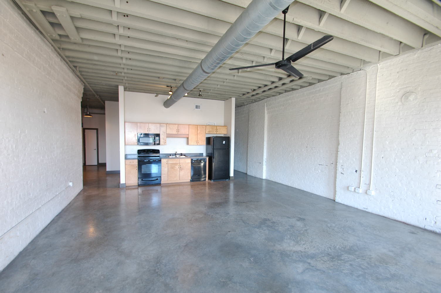 an empty room with a kitchen and a ceiling fan