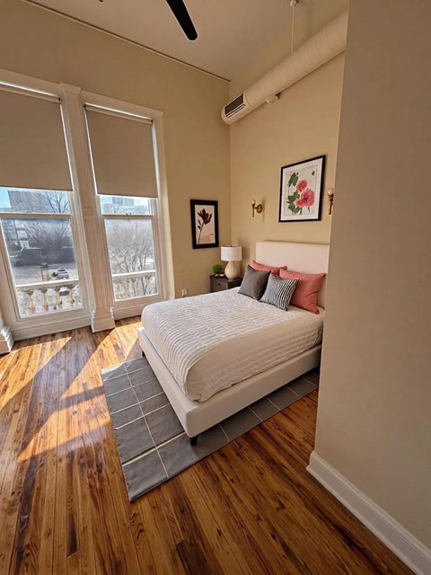A bedroom with a bed, pillows, a lamp, and a window with blinds.