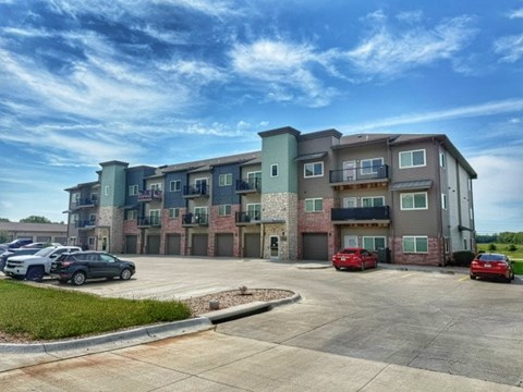 A parking lot in front of a multi-story apartment building with cars parked.