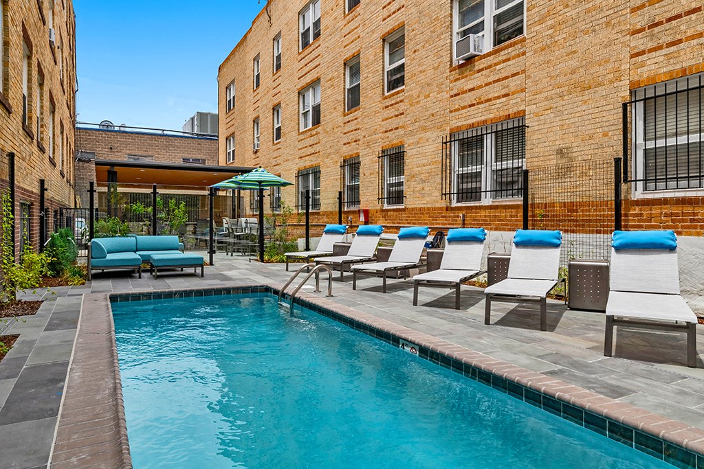a swimming pool with lounge chairs in front of a brick building