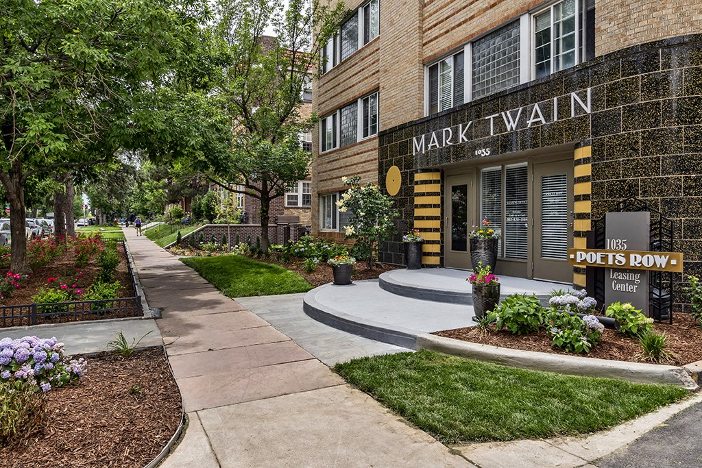 a sidewalk in front of a building with plants and trees