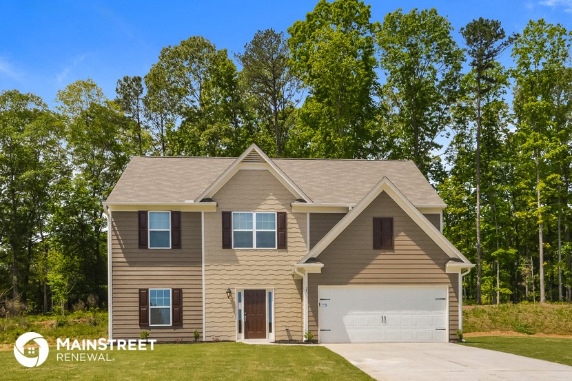 a tan house with a garage and trees in the background