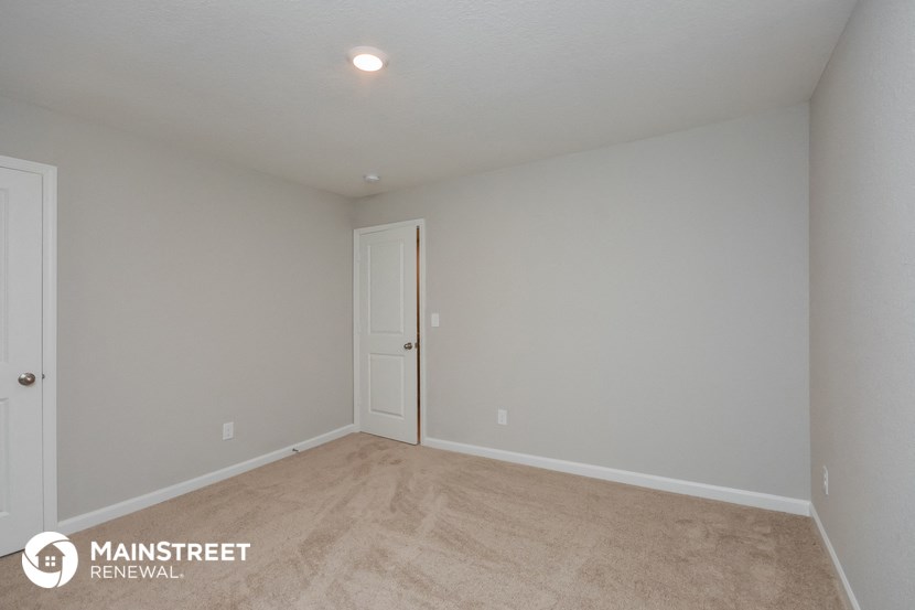 the spacious living room with white walls and beige carpet
