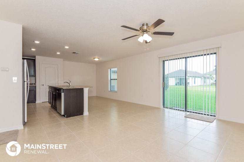 an empty living room with a kitchen and a ceiling fan