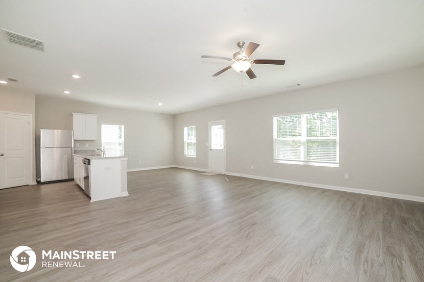 an empty living room with a ceiling fan and a kitchen