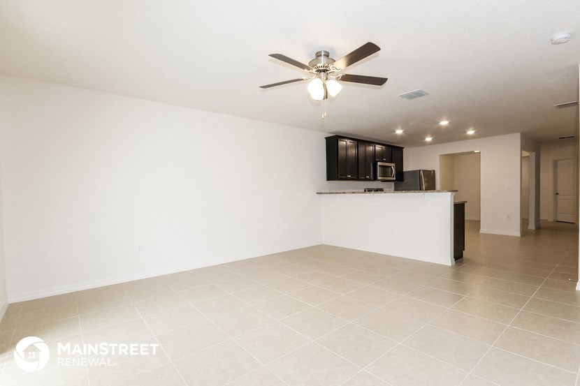 an empty living room with a kitchen and a ceiling fan