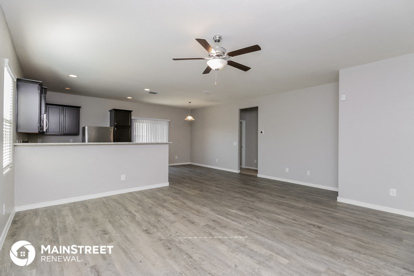 an empty living room with a ceiling fan and a kitchen