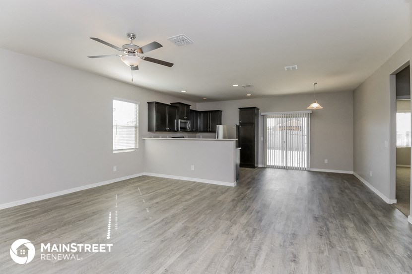 an empty living room with a kitchen and a ceiling fan