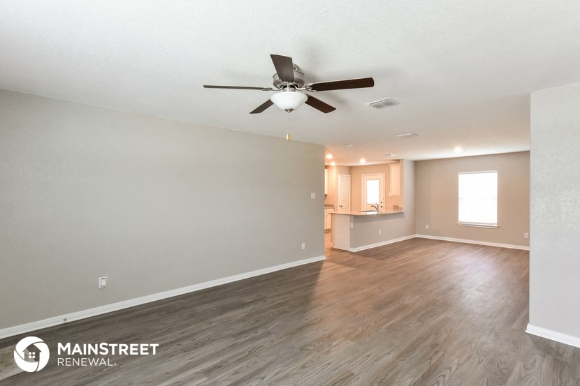 the living room and kitchen of an empty house with a ceiling fan