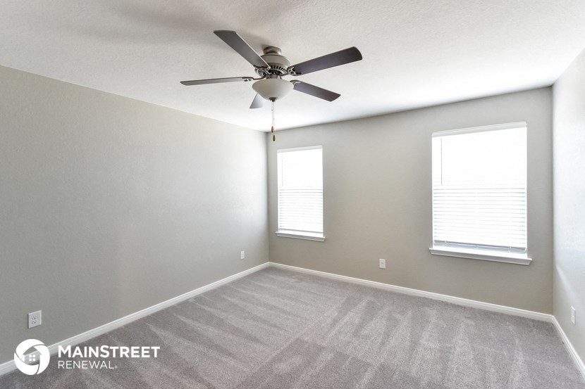 an empty room with a ceiling fan and two windows