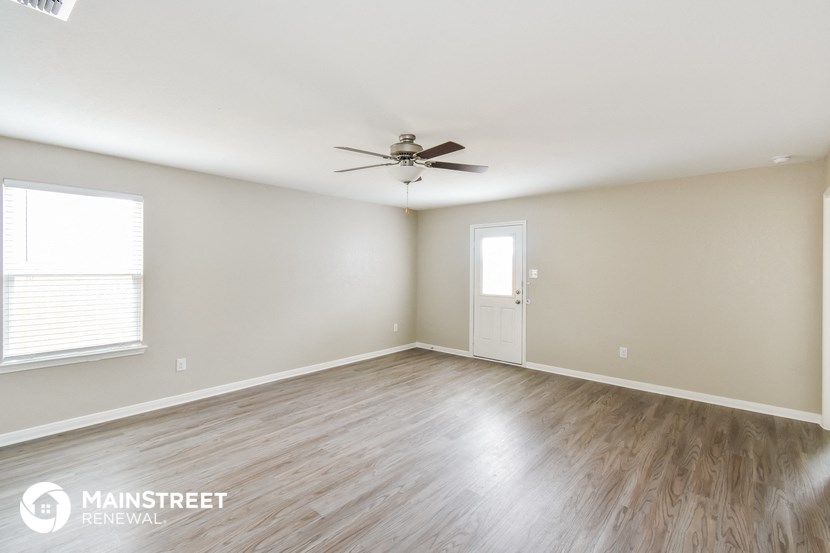 the spacious living room with hardwood floors and a ceiling fan