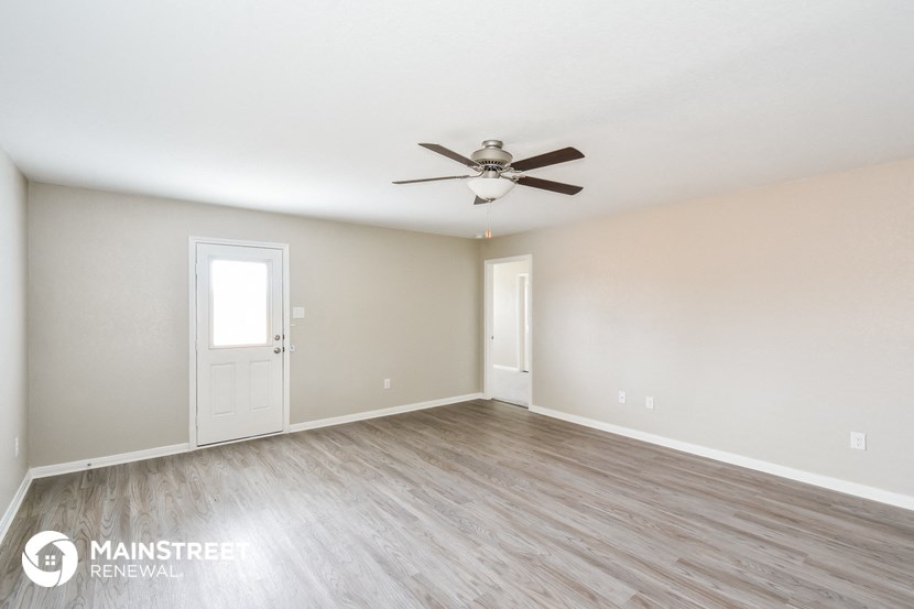 the spacious living room with wood flooring and a ceiling fan