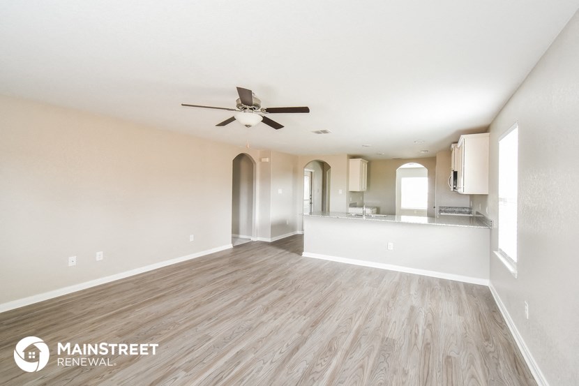 the living room and kitchen of an apartment with wood flooring and a ceiling fan