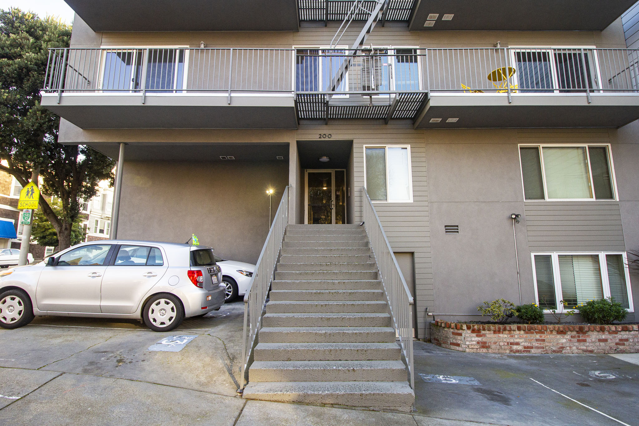 A silver car is parked in front of a two-story building with a staircase leading to the entrance.