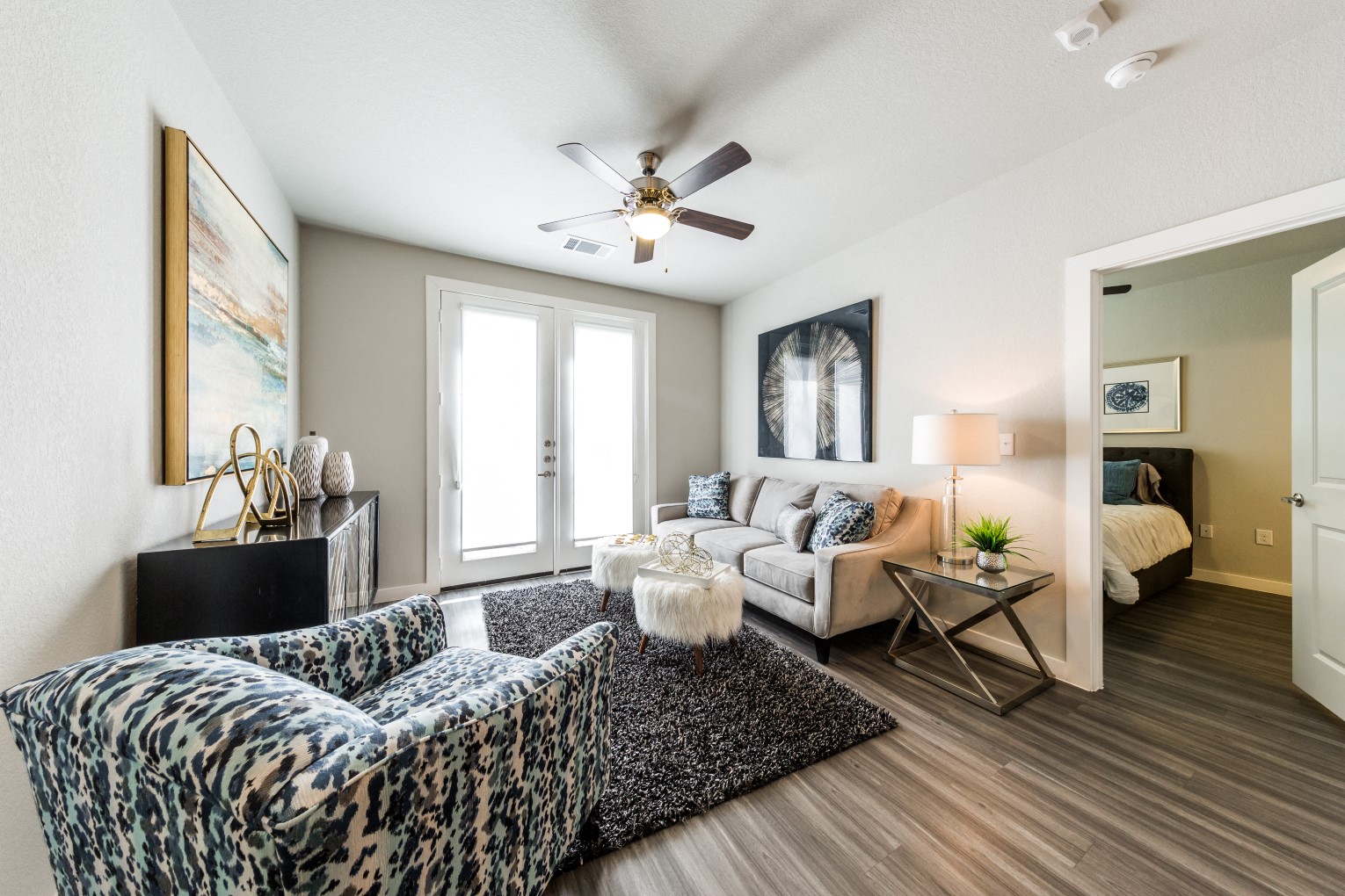 Living room with wood-style flooring, balcony/patio access, ceiling fan, with doorway to bedroom