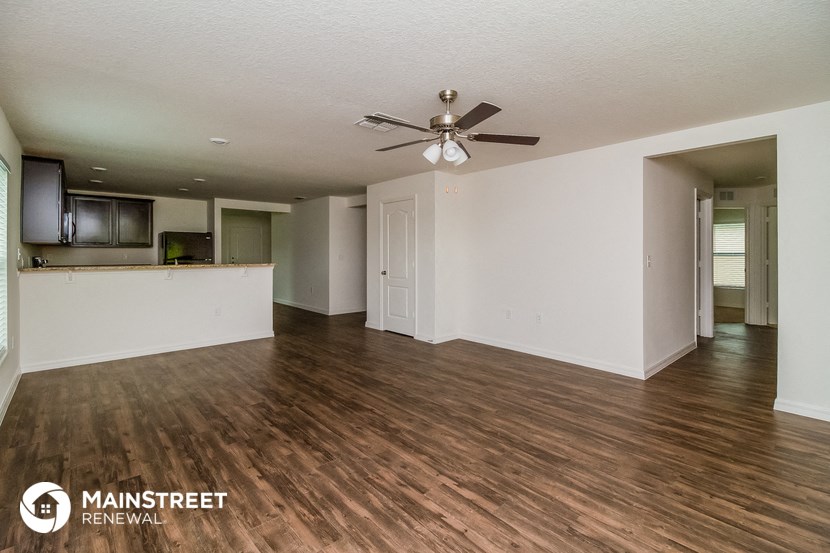 an empty living room with a ceiling fan and a kitchen
