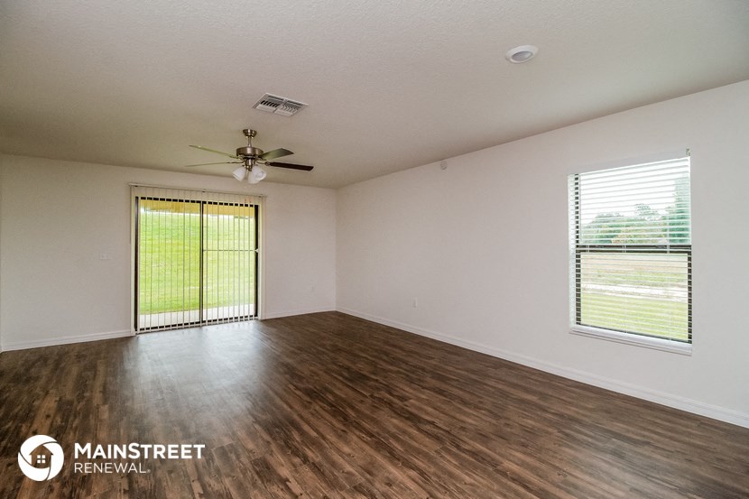 the spacious living room with wood flooring and a ceiling fan