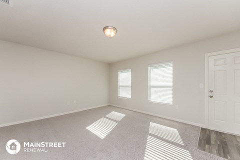 the spacious living room of an apartment with a white door and window