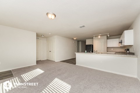 an empty living room and kitchen with white cabinets and a counter top