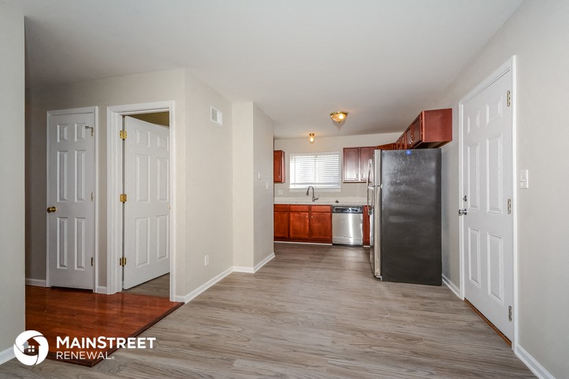 the living room and kitchen of an apartment with white walls and wood floors