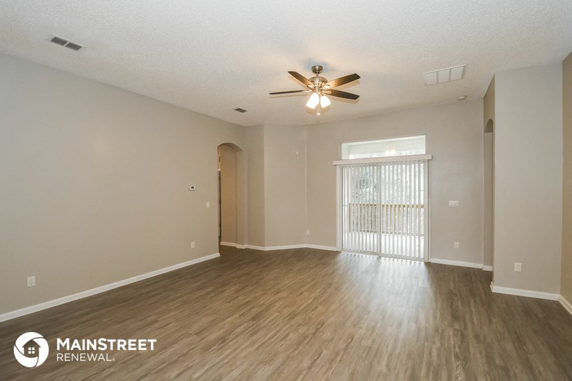 the spacious living room with wood flooring and a ceiling fan