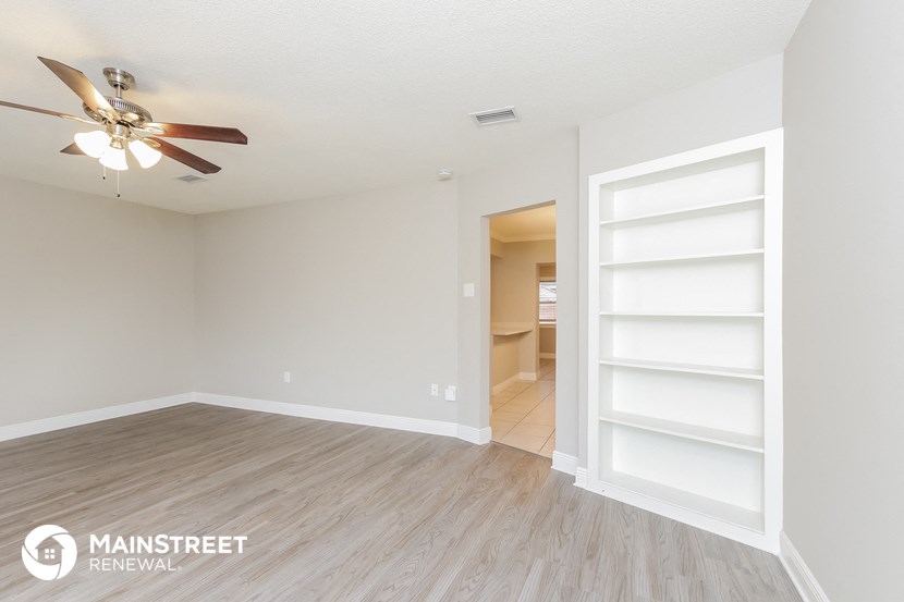 an empty living room with a ceiling fan and white shelves