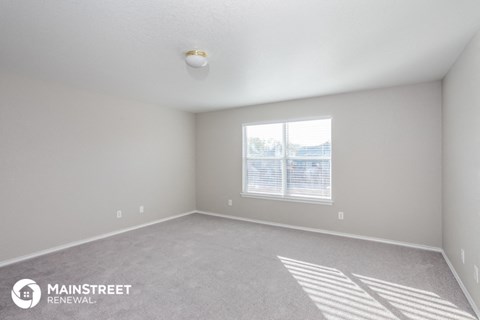 the living room of an apartment with carpet and a window